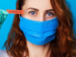 woman in blue mask holding orange covid 19 stick